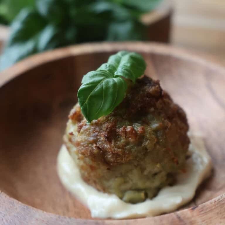 A pesto chicken meatball over garlic aioli with basil on top.
