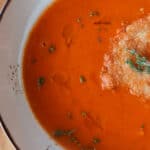 Healthy roasted tomato soup in a bowl topped with olive oil and fresh thyme.