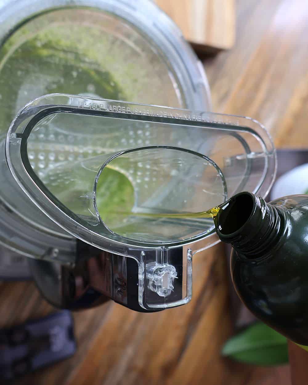 Pouring extra-virgin olive oil through the feed tube of a food processor while making pesto