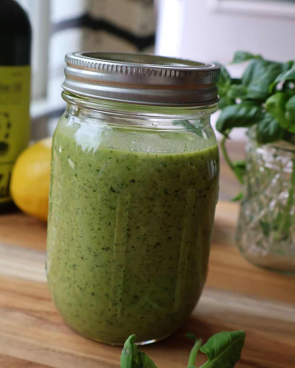 Finished basil walnut pesto in a glass jar with basil leaves and lemon in the background