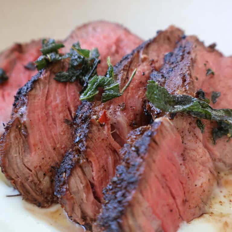 blackened filet mignon sliced on a plate with cauliflower puree and sage brown butter