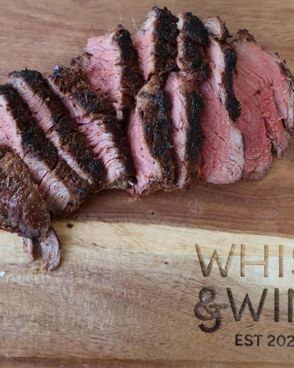 sliced blackened filet mignon on Whisk and Wine cutting board showing perfect pink center