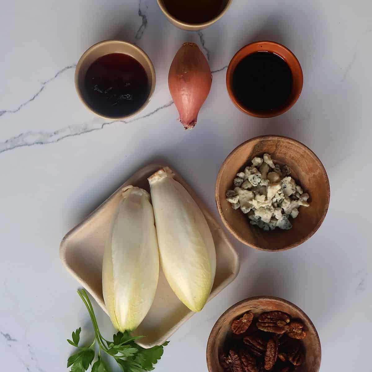 Flat lay of endive salad ingredients on marble: Belgian endive, Gorgonzola, balsamic vinegar, olive oil, honey, shallot, and strawberries