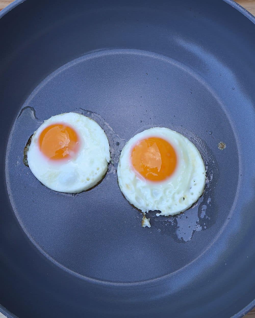 Two fried eggs cooking in butter in a non-stick skillet
