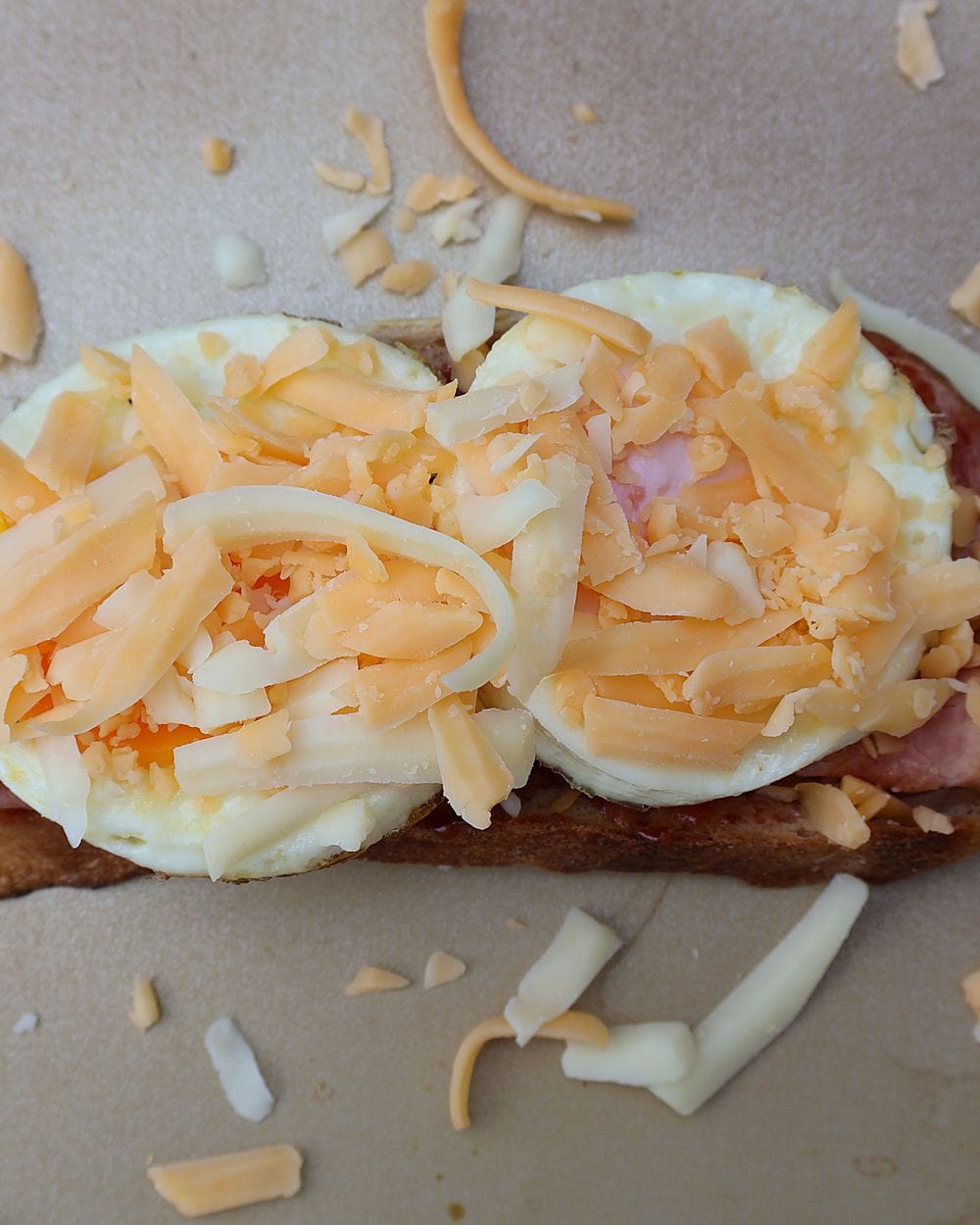 Assembled fried egg sandwich with eggs, ham, and cheese on a sheet pan ready to broil