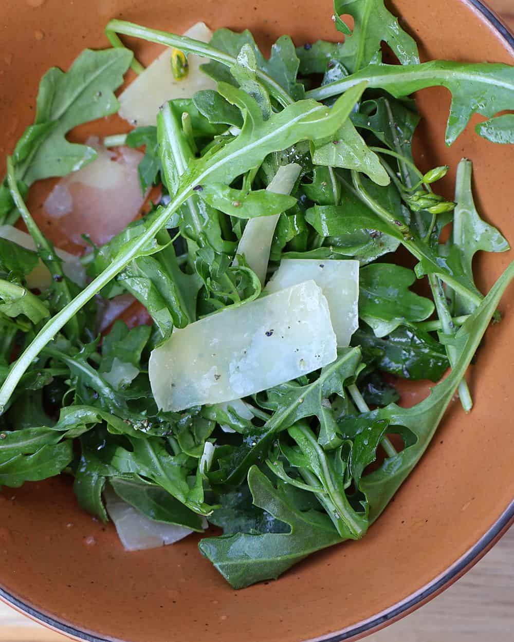 Fresh arugula salad tossed with lemon juice and olive oil in a bowl