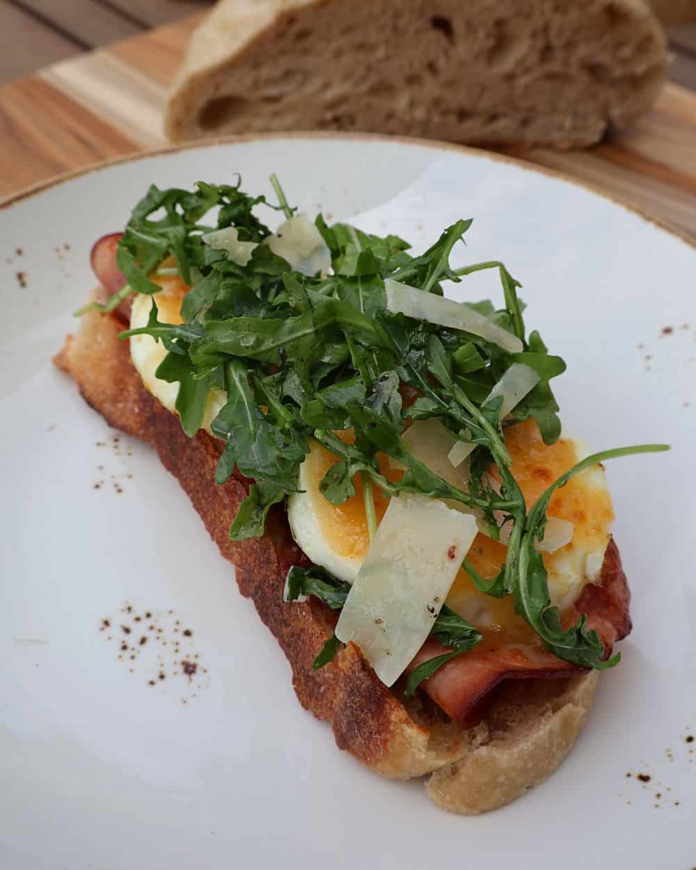 Finished open-face fried egg sandwich topped with arugula and parmesan shavings on a white plate