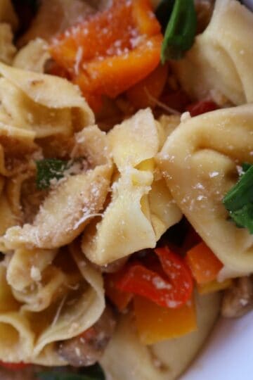 roasted vegetable tortellini salad in a white bowl topped with basil