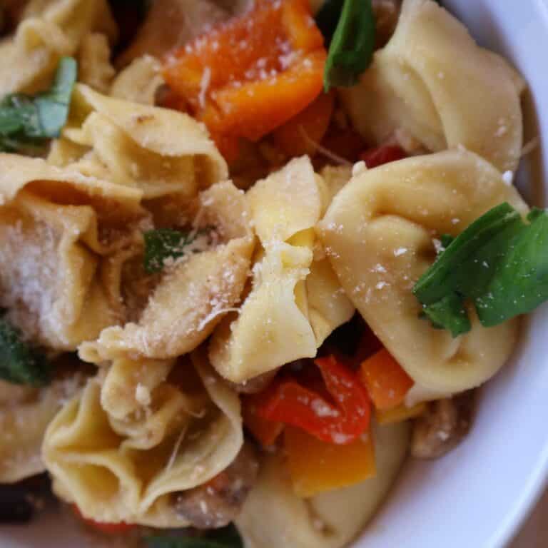 roasted vegetable tortellini salad in a white bowl topped with basil