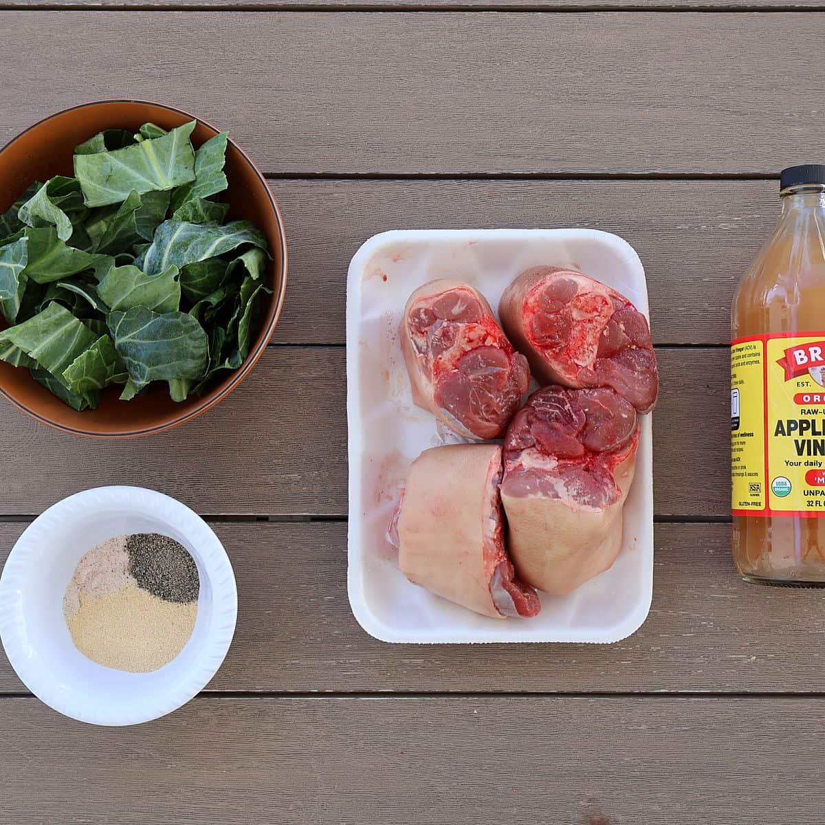 Ingredient flat lay showing collard greens, smoked ham hocks, apple cider vinegar, garlic powder, salt, and pepper