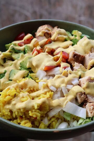 Curry chicken bowl with grilled chicken, yellow rice, and fresh vegetables topped with curry yogurt sauce
