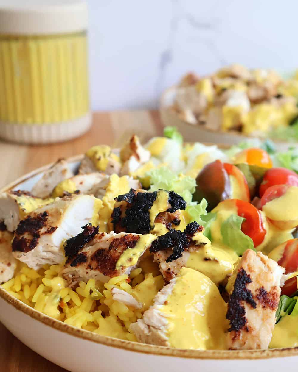 Curry chicken bowl with grilled chicken, yellow rice, romaine lettuce, tomatoes, and red onion drizzled with curry yogurt sauce