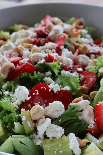 Strawberry salad with gorgonzola, cucumber, and almonds in a white bowl, topped with homemade strawberry balsamic dressing