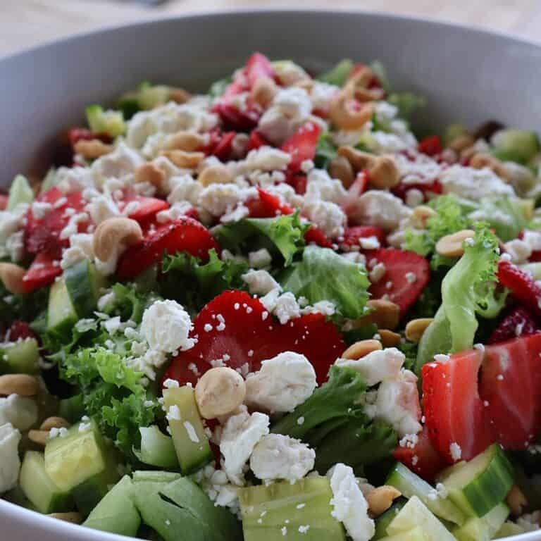 Strawberry salad with gorgonzola, cucumber, and almonds in a white bowl, topped with homemade strawberry balsamic dressing