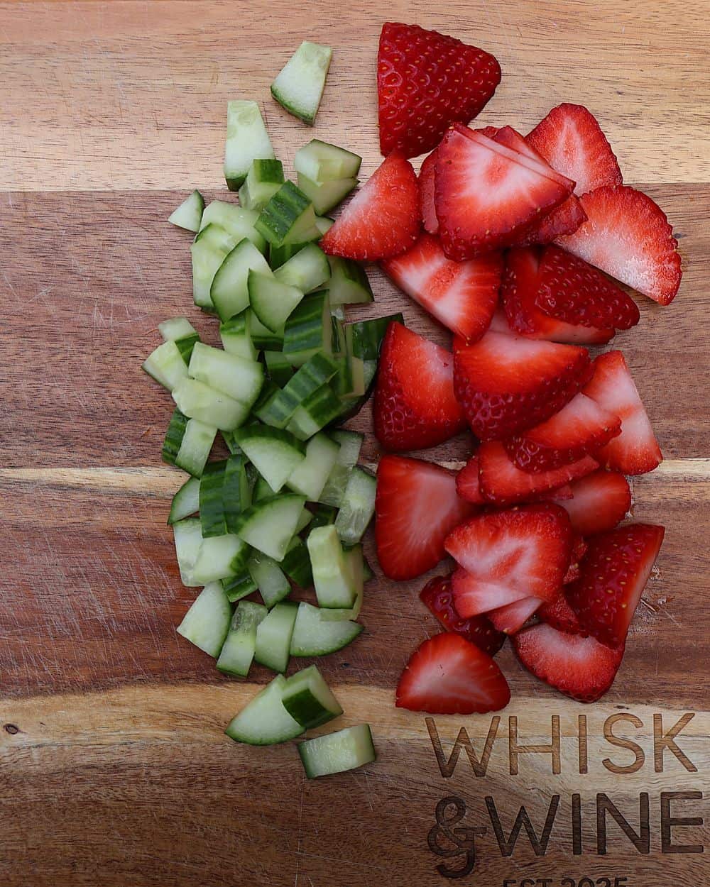 Sliced strawberries and chopped cucumber on a cutting board