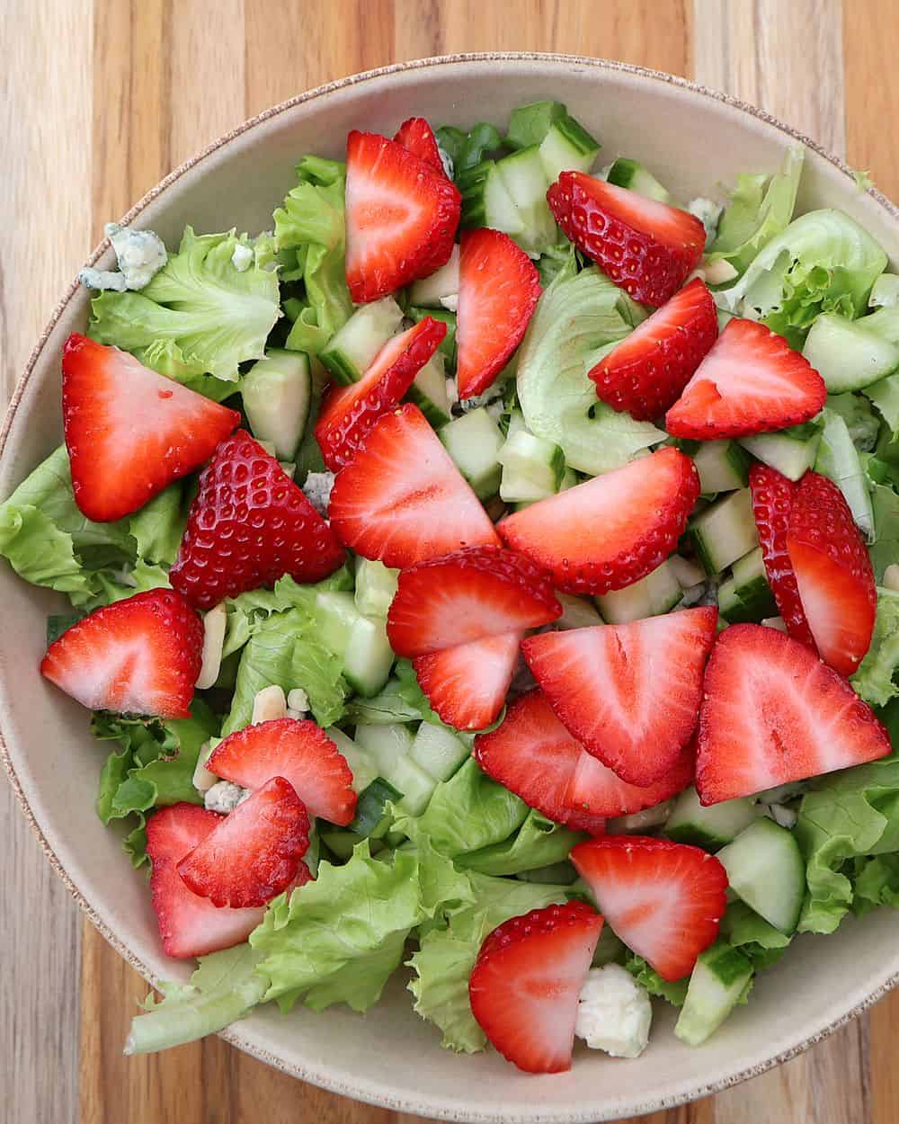 Assembling strawberry salad with gorgonzola and almonds in a bowl