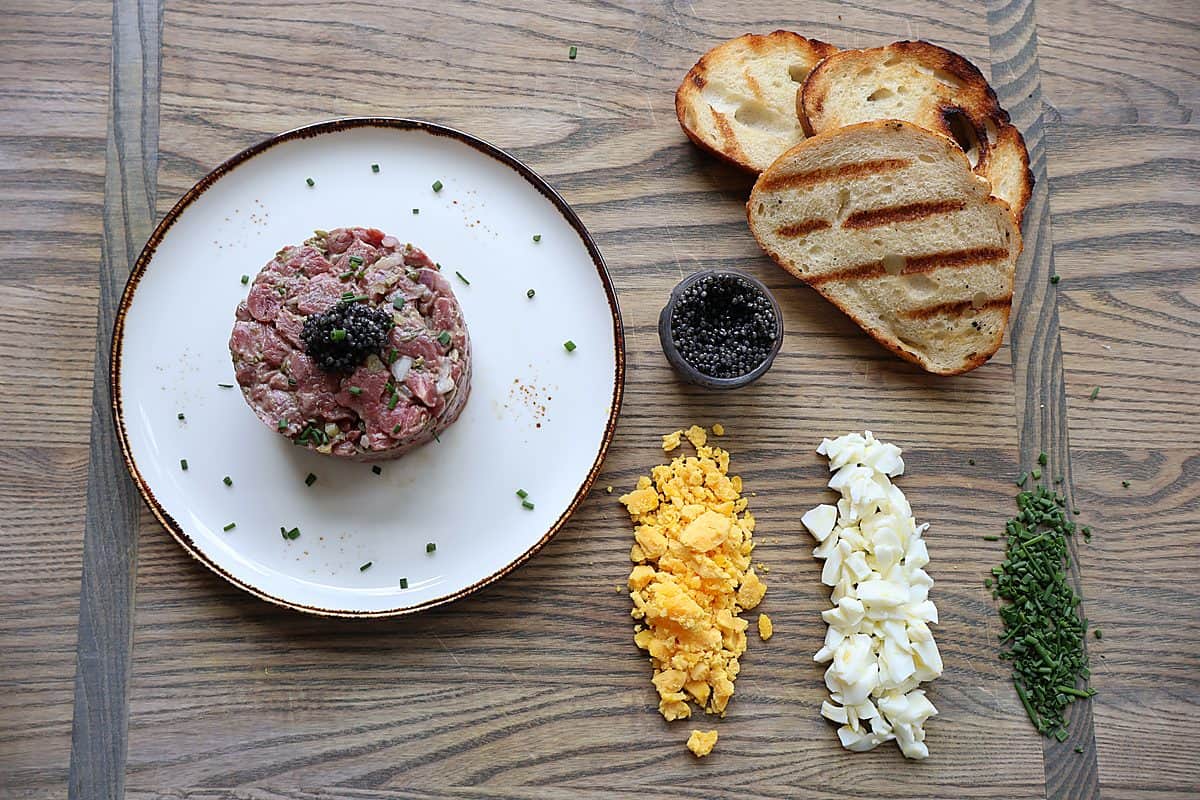Beef tartare ingredients flat-lay: filet mignon, shallot, capers, cornichons, Dijon mustard, Worcestershire sauce
