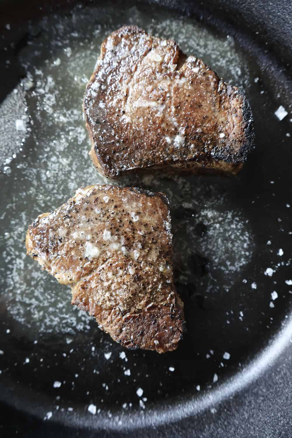 Sliced cast iron filet mignon on a wood board with a blushing medium-rare center, melting compound butter, and flaky sea salt