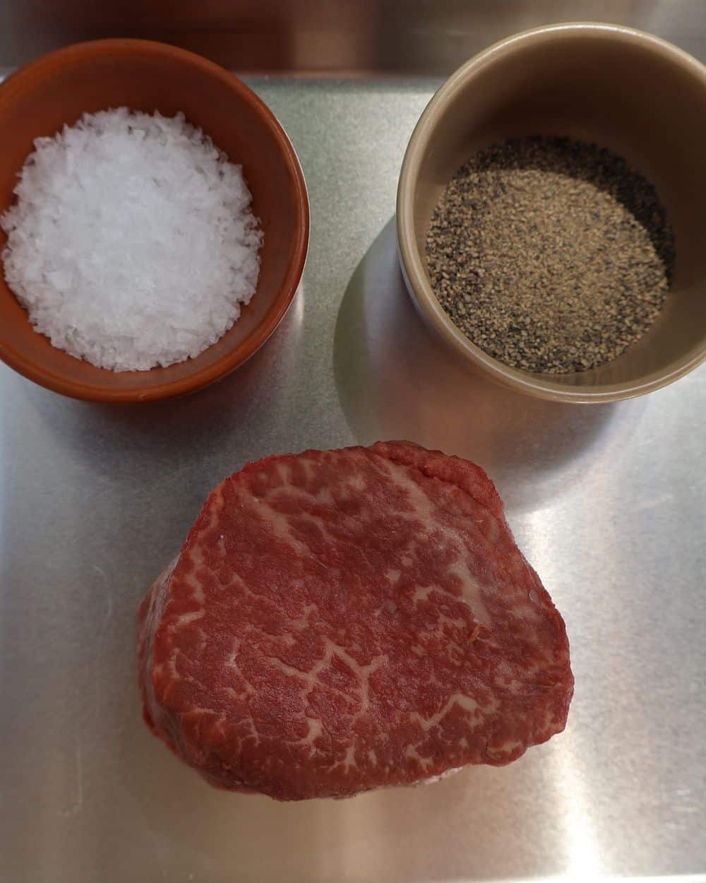 Two center-cut filet mignon steaks patted dry and seasoned with kosher salt and pepper on a board