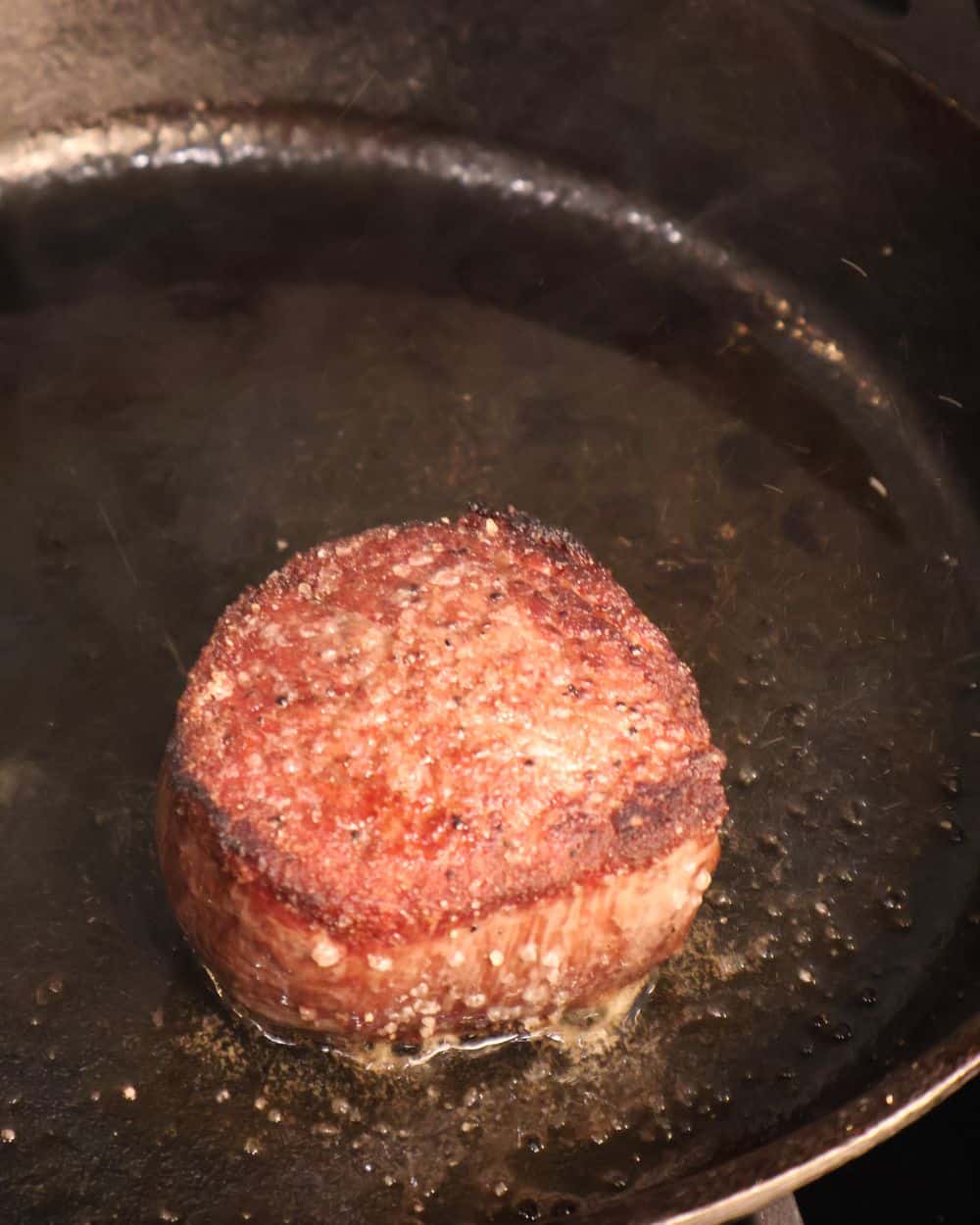 Filet mignon searing in a smoking-hot cast iron skillet with a deep brown crust forming