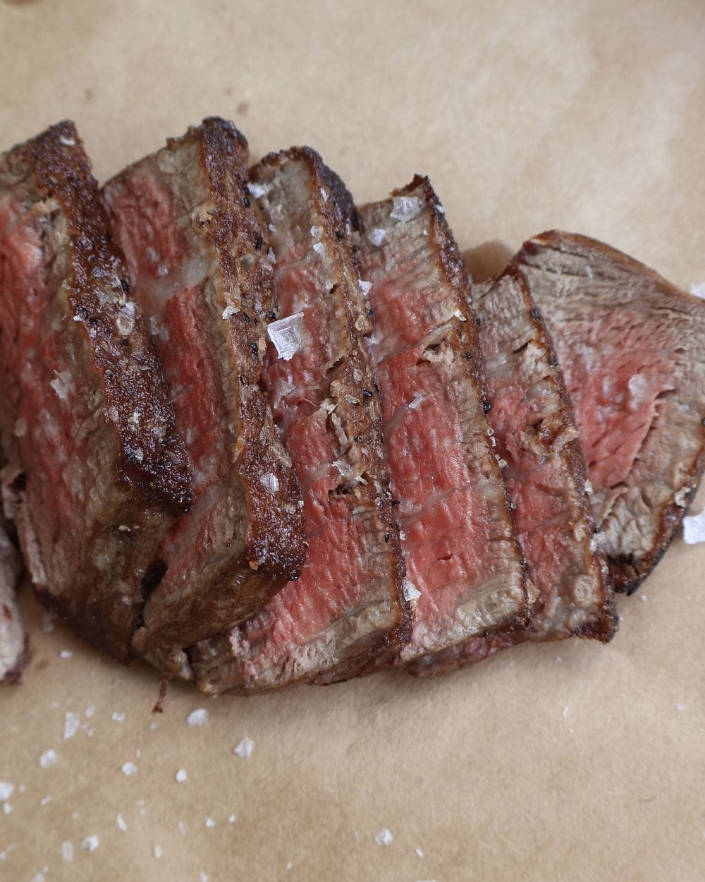 Rested filet mignon topped with flaky sea salt and a melting medallion of compound butter on a wood board