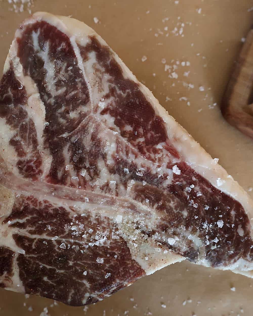 Dry aged porterhouse steak salted heavily on a wire rack over a sheet pan, dry brining in the fridge