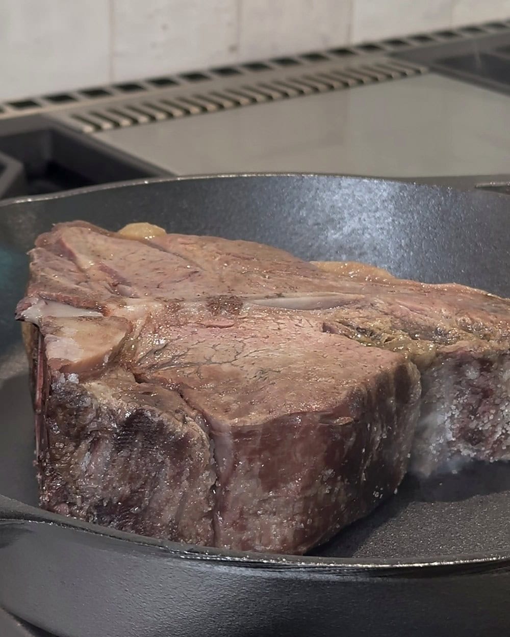 Dry aged porterhouse pressed into a smoking-hot cast iron skillet for the final sear, hard dark crust forming