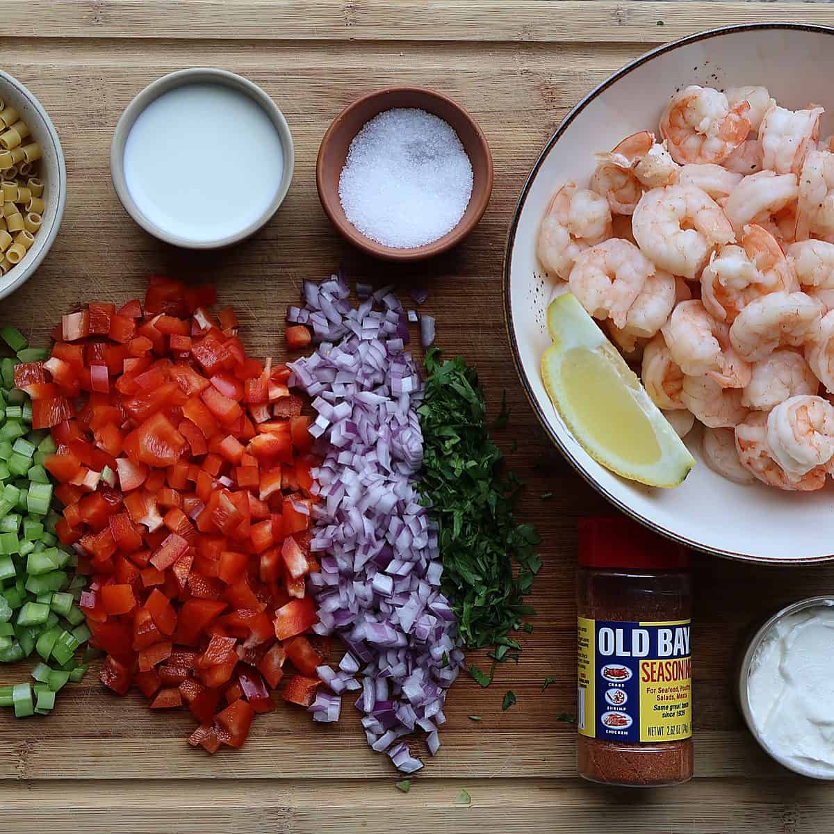 Old Bay shrimp macaroni salad ingredients flat lay - shrimp, elbow macaroni, Old Bay seasoning, mayo, sour cream, celery, red pepper, red onion, lemon, milk