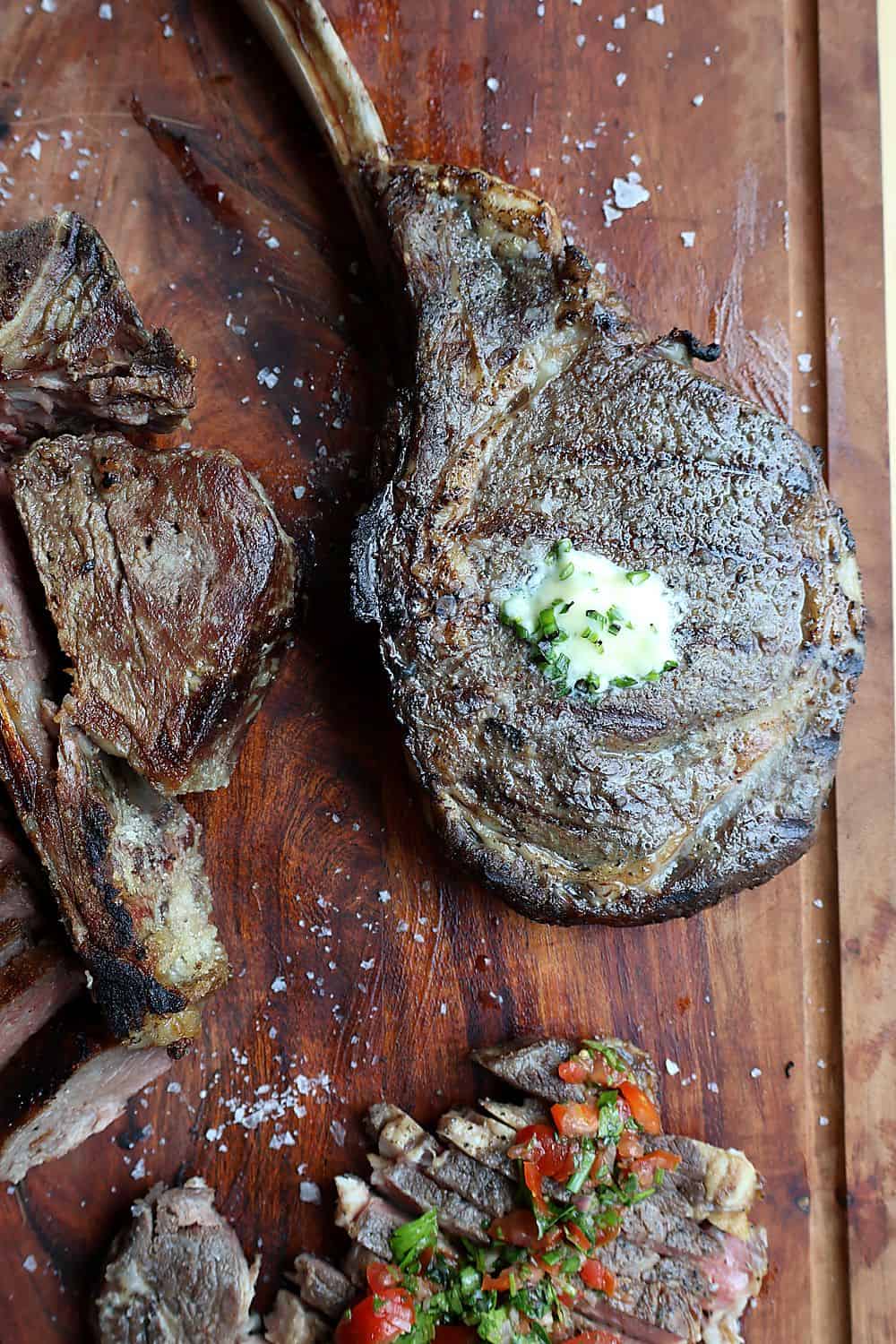 Sliced reverse sear tomahawk steak on an end-grain wood board with melted compound butter and Florida Pure Sea Salt flakes