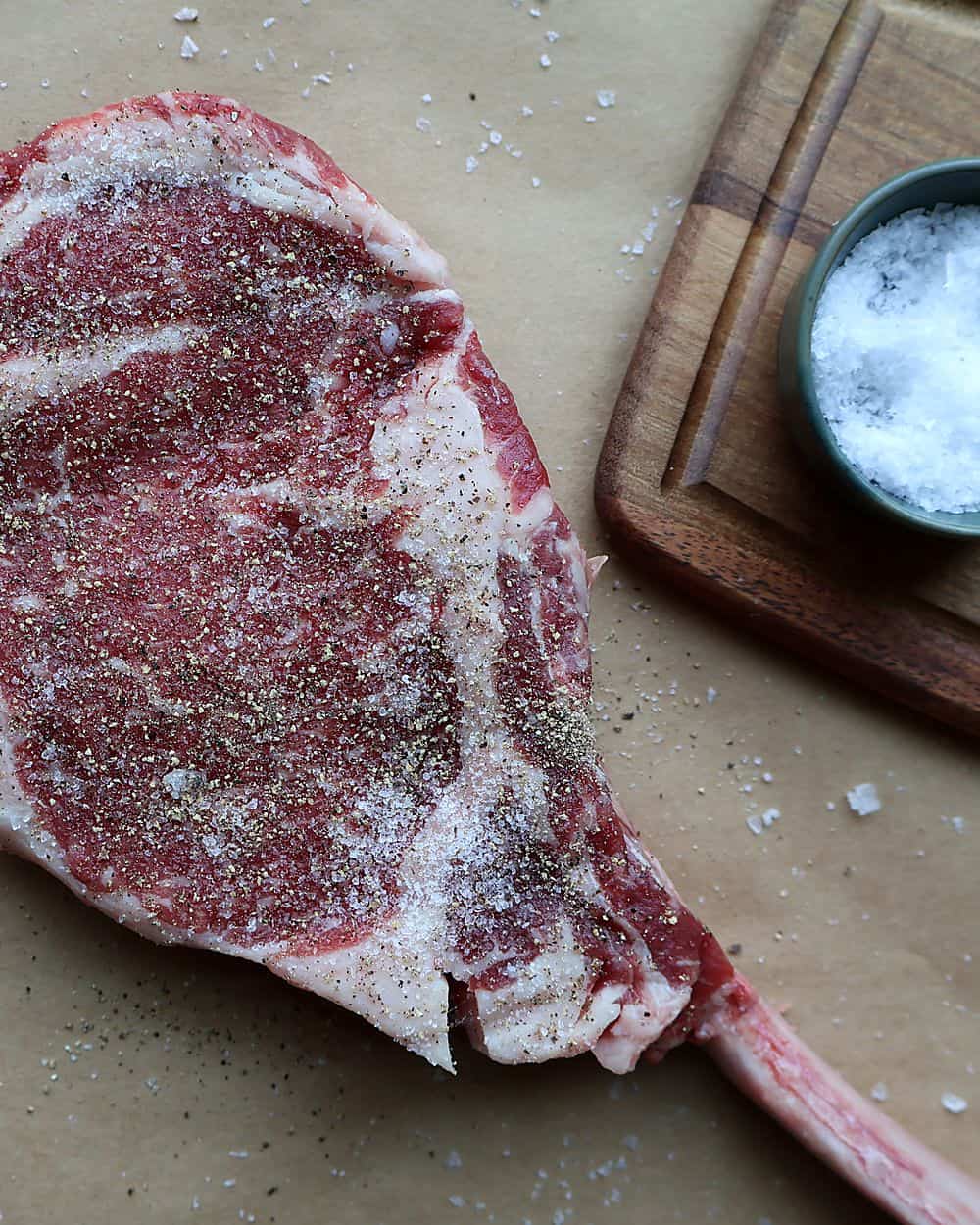 Raw tomahawk steak on a wire rack, generously salted, dry brining
