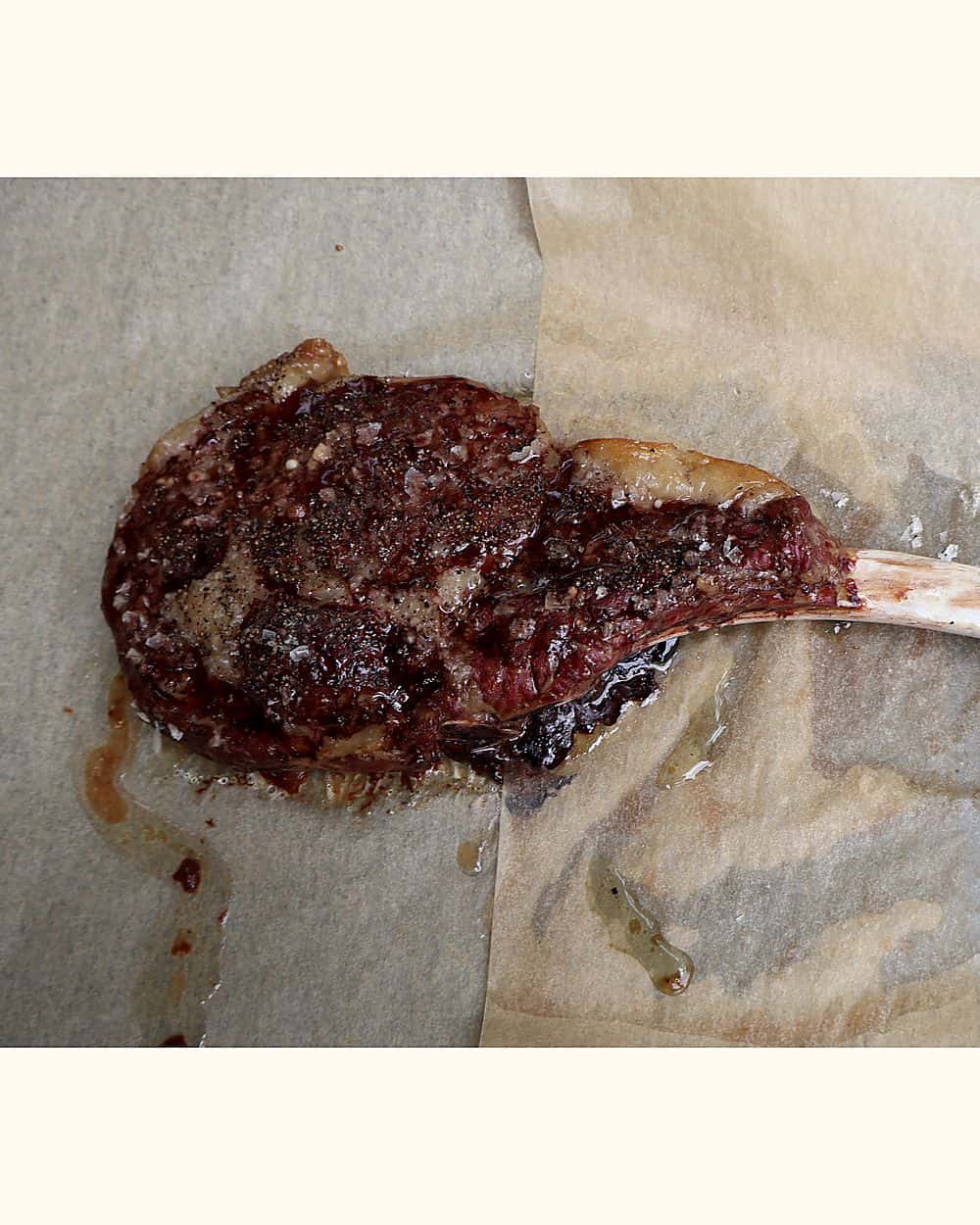 Cooked tomahawk steak coming out of the 225°F oven on a sheet pan with leave-in probe reading 115°F