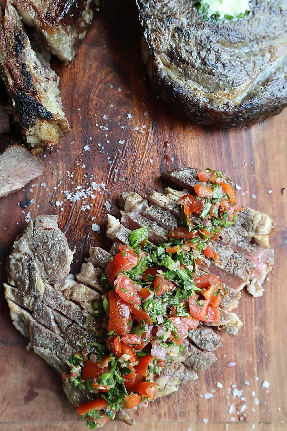 Sliced sous vide ribeye topped with tomato chimichurri and Maldon salt on a wooden board