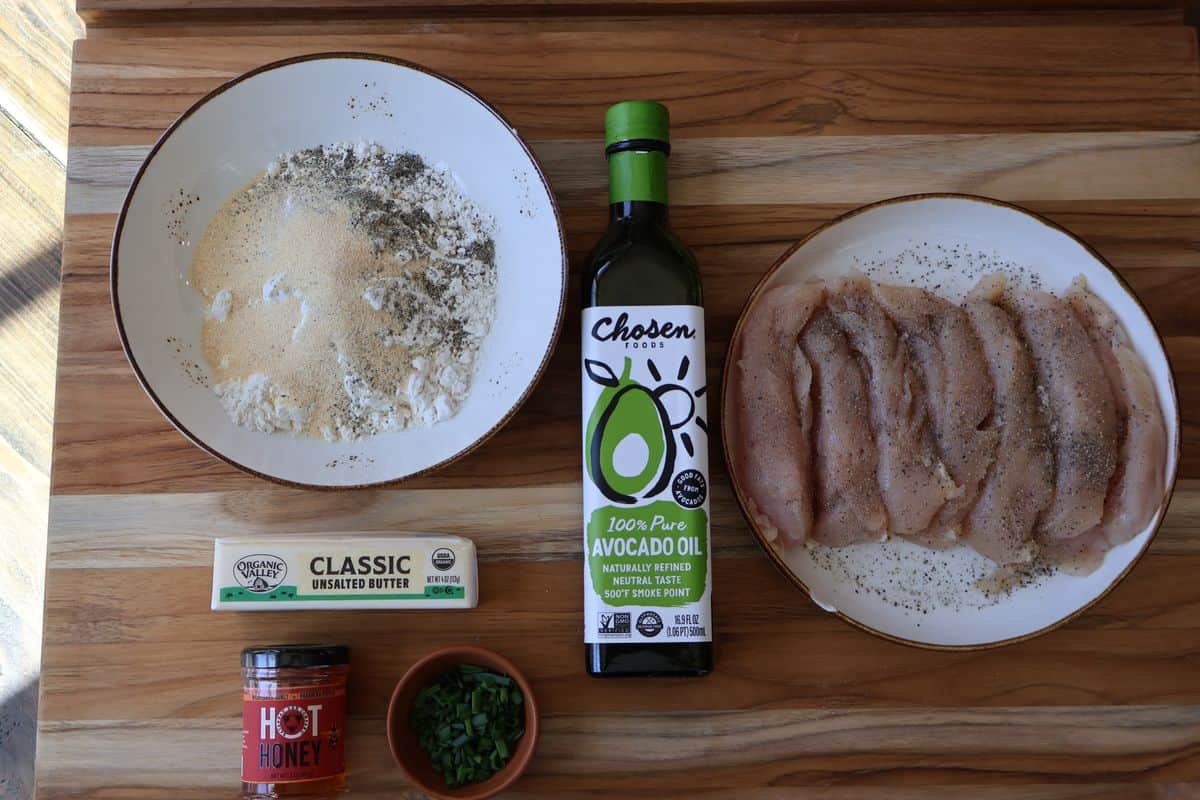Ingredients for spicy chicken and waffles in small bowls — chicken tenders, flour, eggs, Frank’s RedHot, butter, salt, garlic powder, pepper