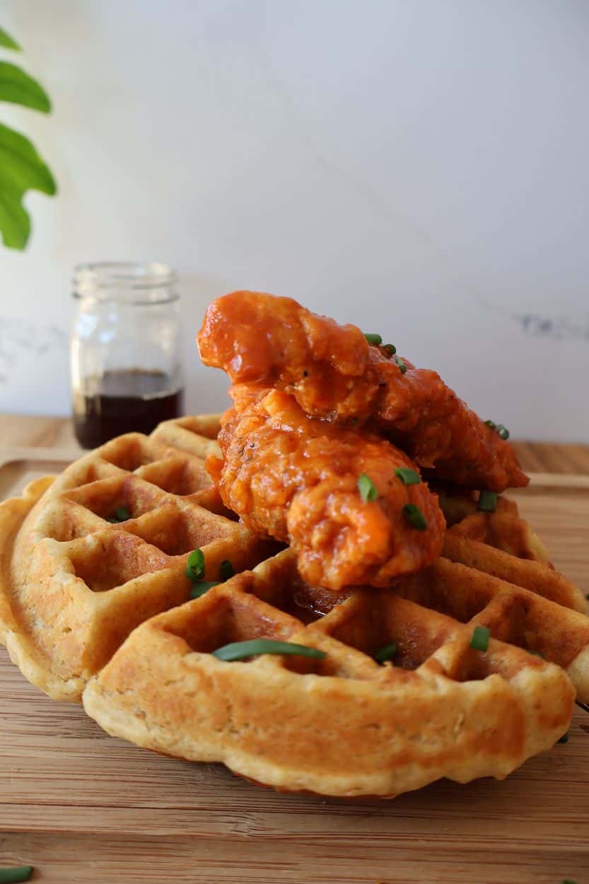 Spicy chicken tenders tossed in buttery hot sauce and plated on a waffle with maple syrup and chives