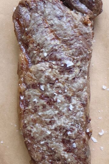 Seared Wagyu strip steak with flaky salt on butcher paper, sliced to show the marbling