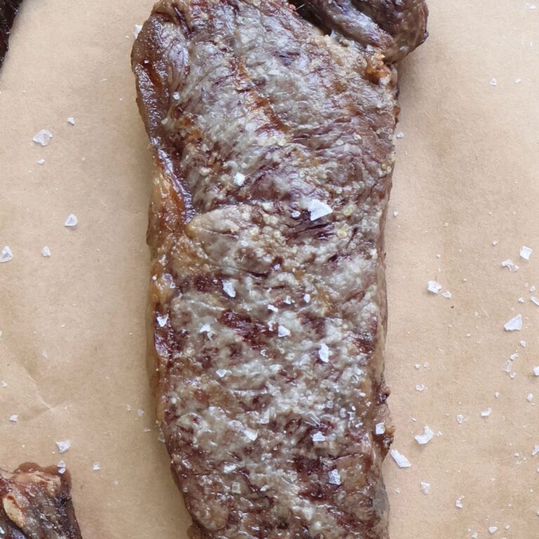 Seared Wagyu strip steak with flaky salt on butcher paper, sliced to show the marbling