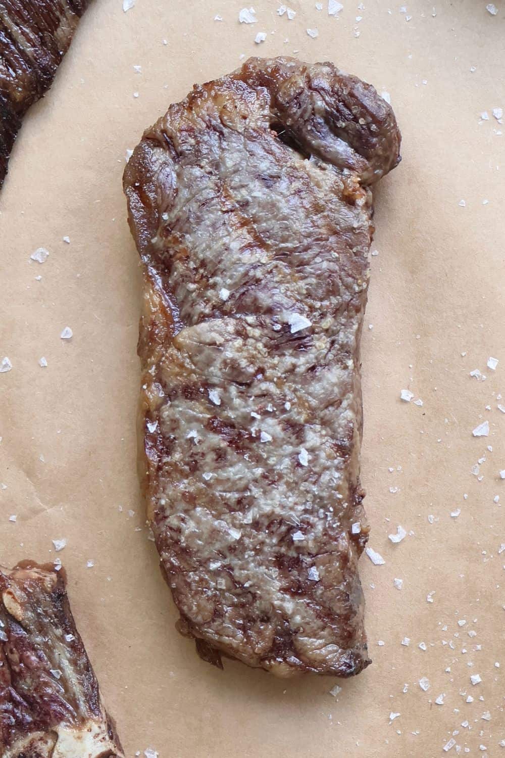 Cooked Wagyu strip steak with flaky salt on butcher paper, vertical hero shot