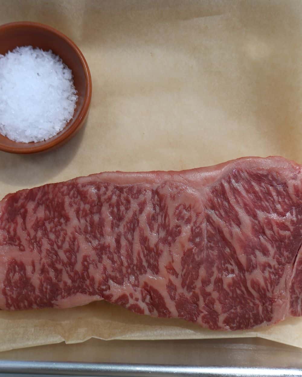 Wagyu strip steak tempering on butcher paper with kosher salt