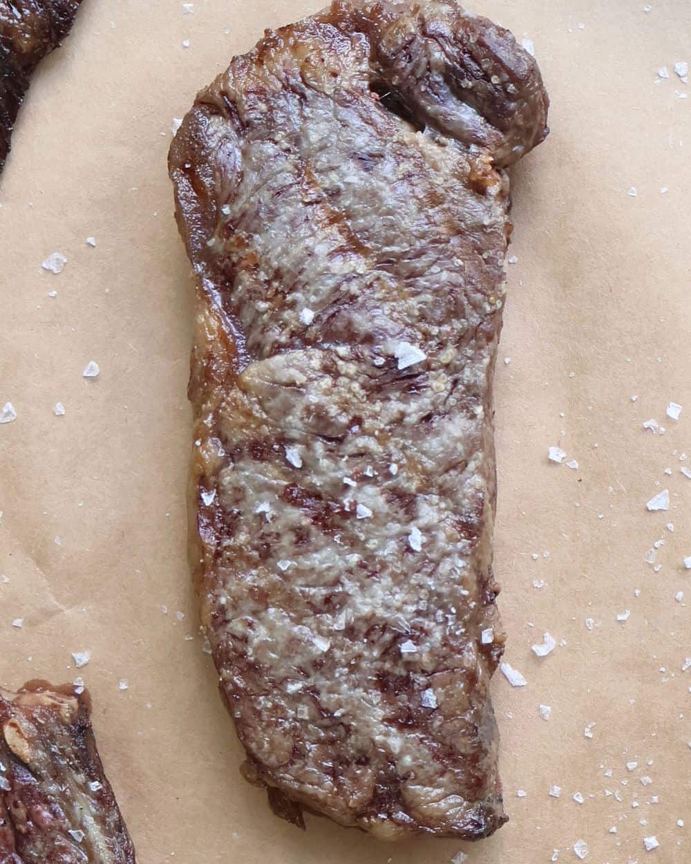 Seared Wagyu strip steak resting on butcher paper with flaky salt