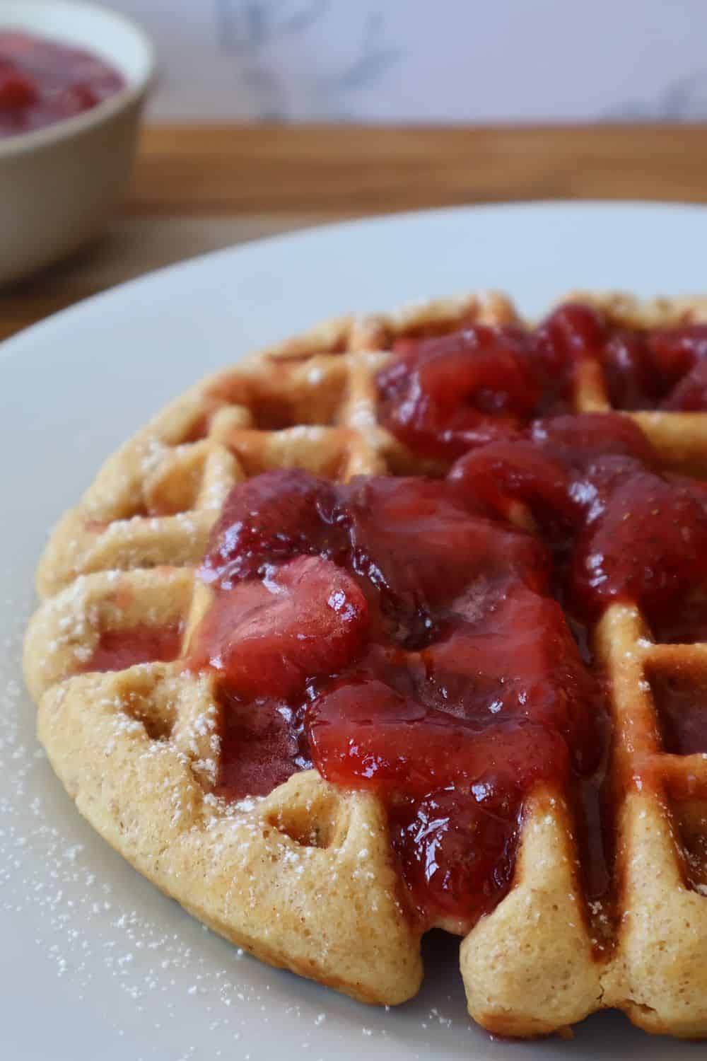 Stack of whole wheat waffles topped with homemade strawberry syrup and powdered sugar