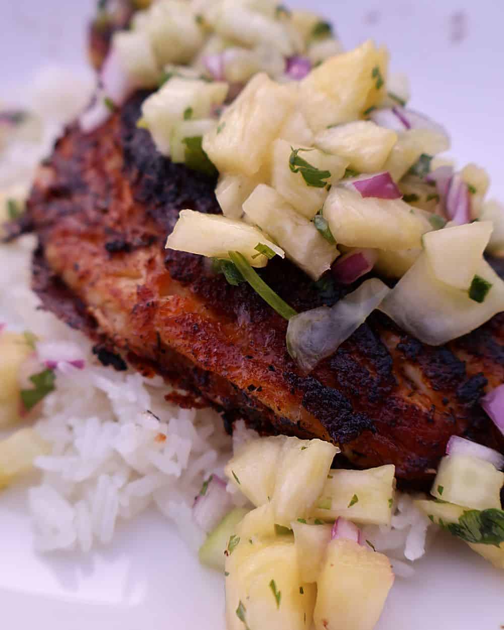 Blackened fish topped with pineapple salsa over rice on a plate