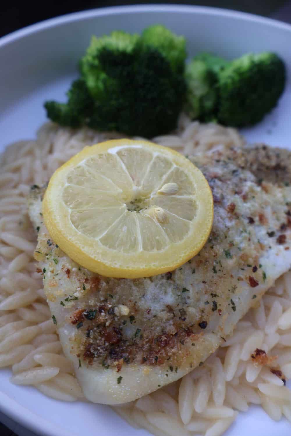 Overhead of parmesan crusted fish on lemon orzo topped with a lemon slice