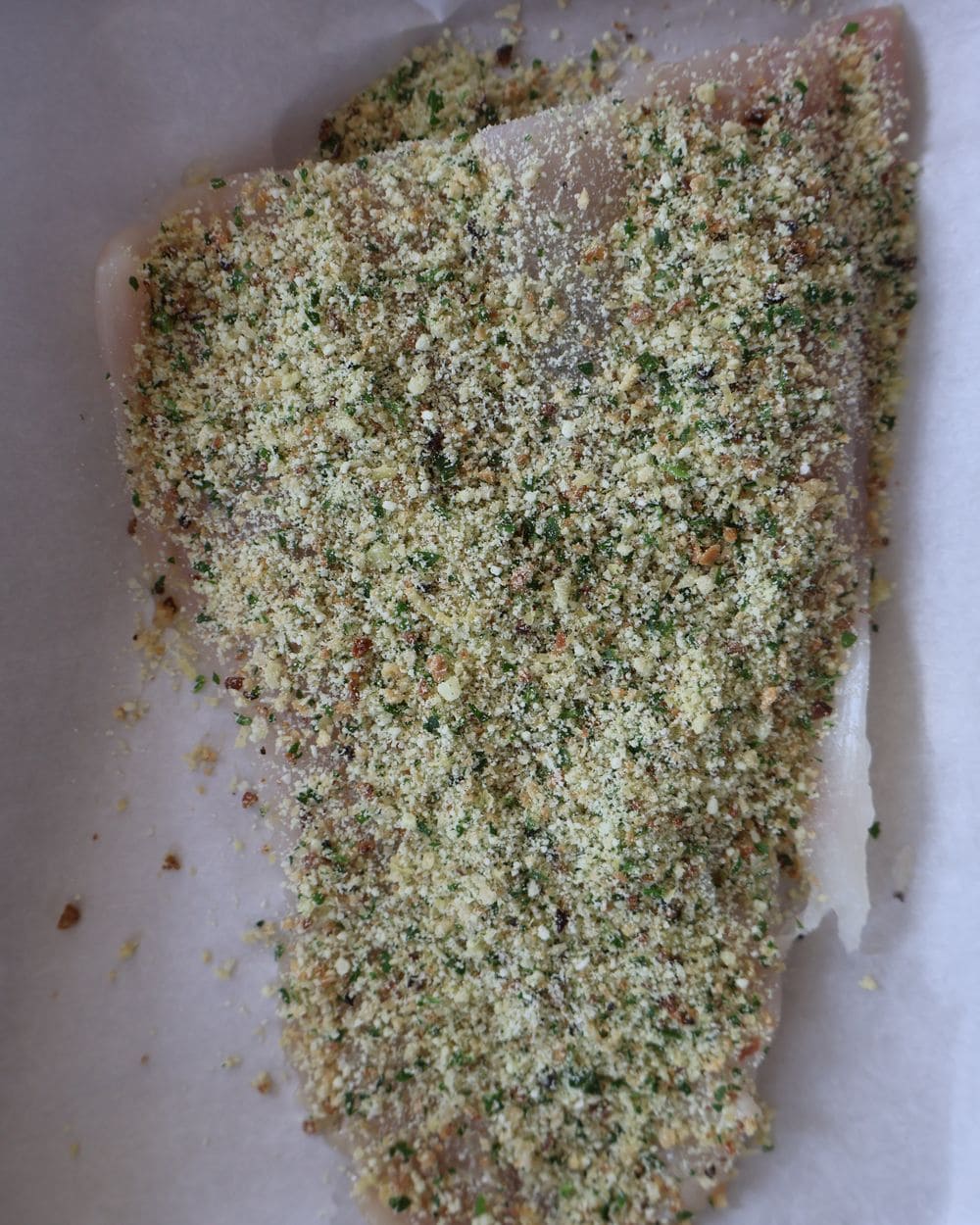 White fish fillet on parchment with the parmesan breadcrumb crust pressed on top