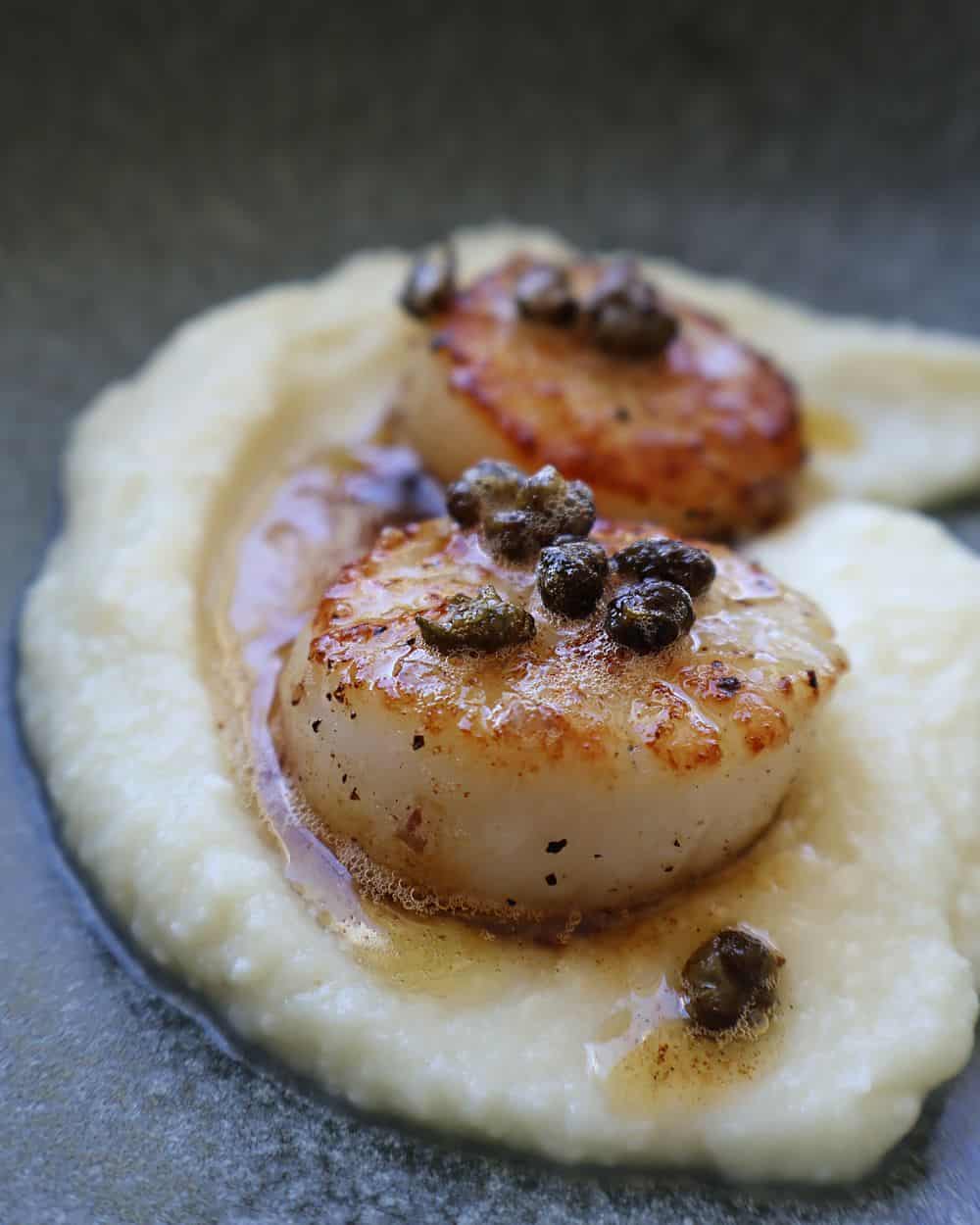 Plated seared scallops on cauliflower puree with caper brown butter spooned over