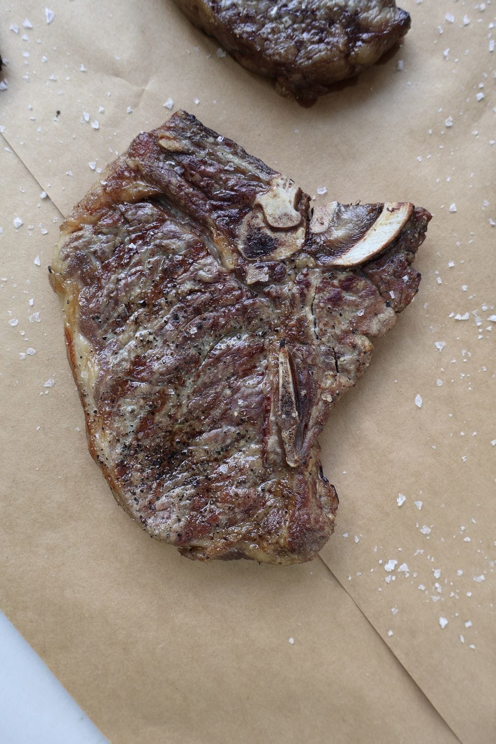 Grilled T-bone steak on a wood board with deep char and the T-shaped bone visible, finished with flaky sea salt