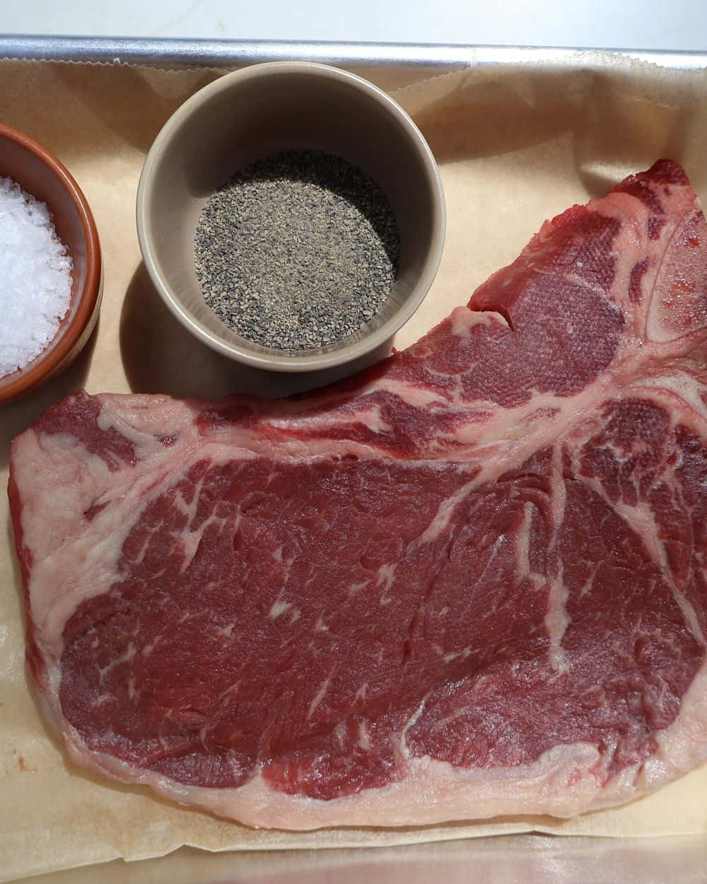 A T-bone steak patted dry and seasoned with kosher salt and pepper on a board