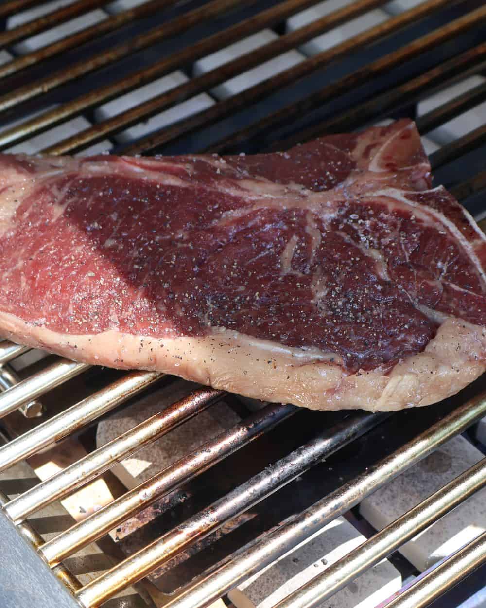 A T-bone steak searing over the hot zone of a grill with a deep, dark crust forming