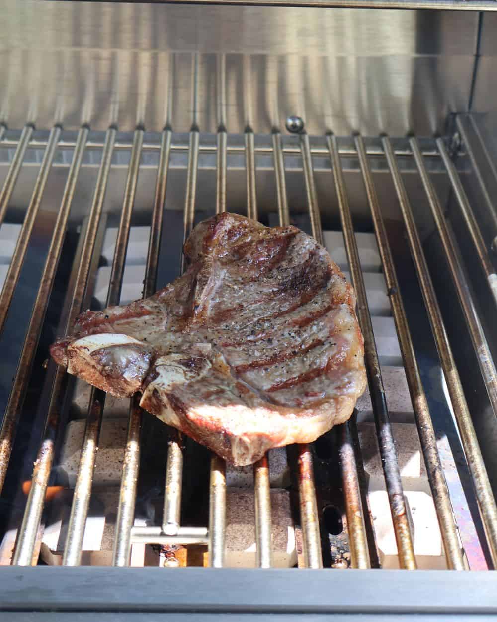 A T-bone finishing over indirect heat with an instant-read thermometer in the strip side