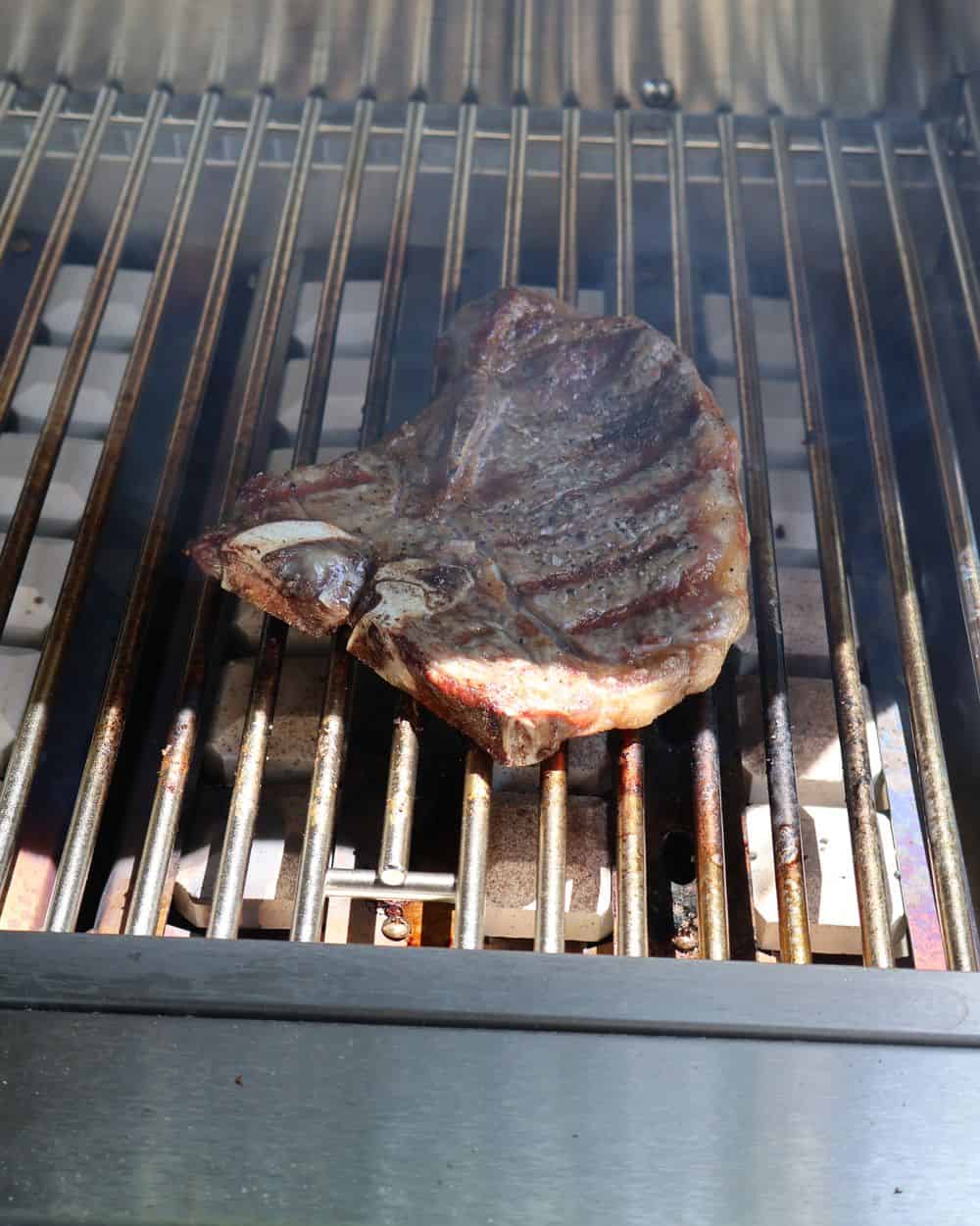 A rested T-bone steak carved off the bone and sliced, finished with flaky sea salt on a wood board