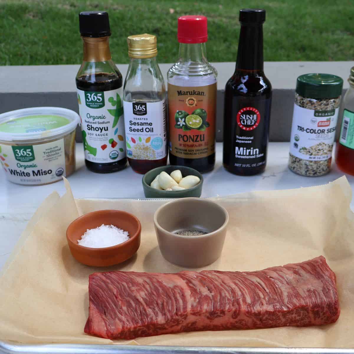 Ingredient flat lay for miso marinated skirt steak with white miso, soy, mirin, ponzu, sesame oil, honey, and a marbled skirt steak